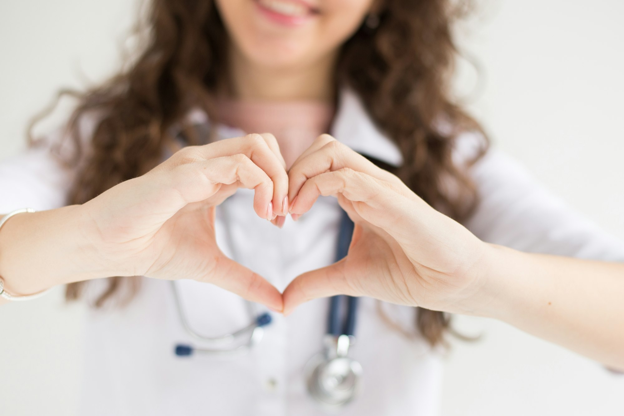 A doctor with his stethoscope shows heart of hands. medical background